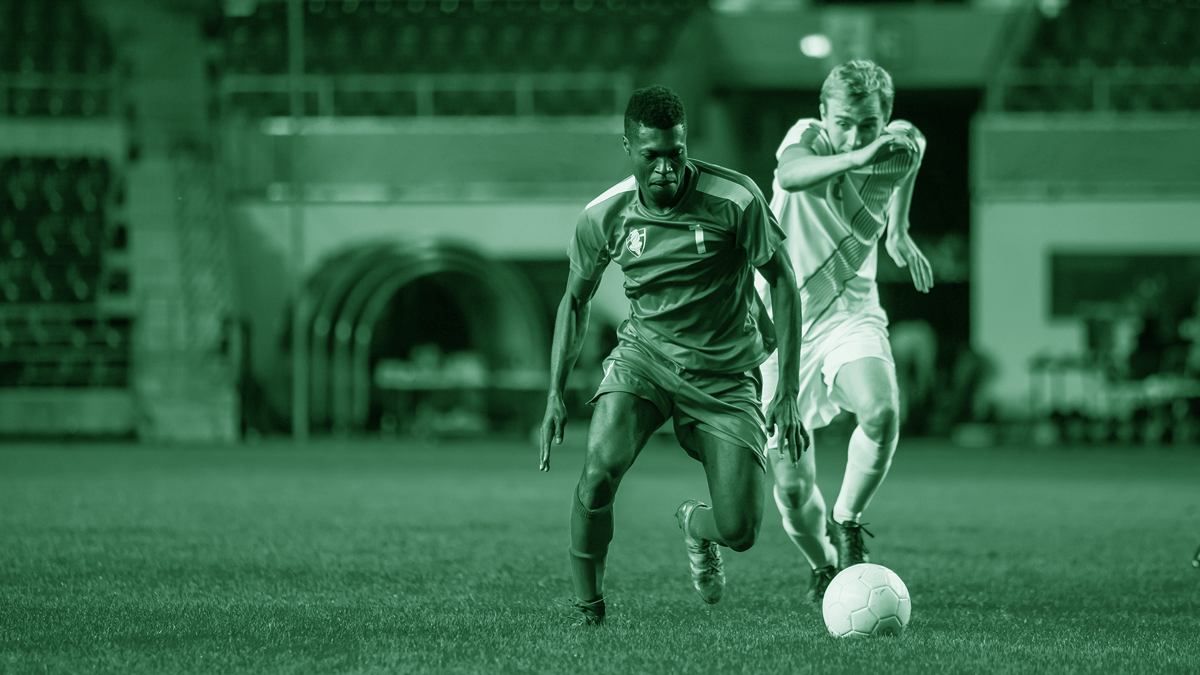 Två fotbollsspelare i intensiv närkamp om bollen under en match på ett upplyst stadion.