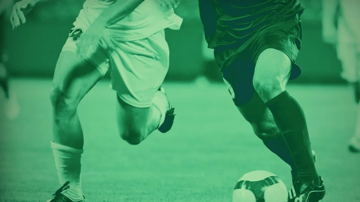 Två fotbollsspelare i närkamp om bollen på planen, fångade i rörelse med en gröntonad färgeffekt.