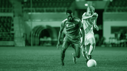 Två fotbollsspelare i intensiv närkamp om bollen under en match på ett upplyst stadion.